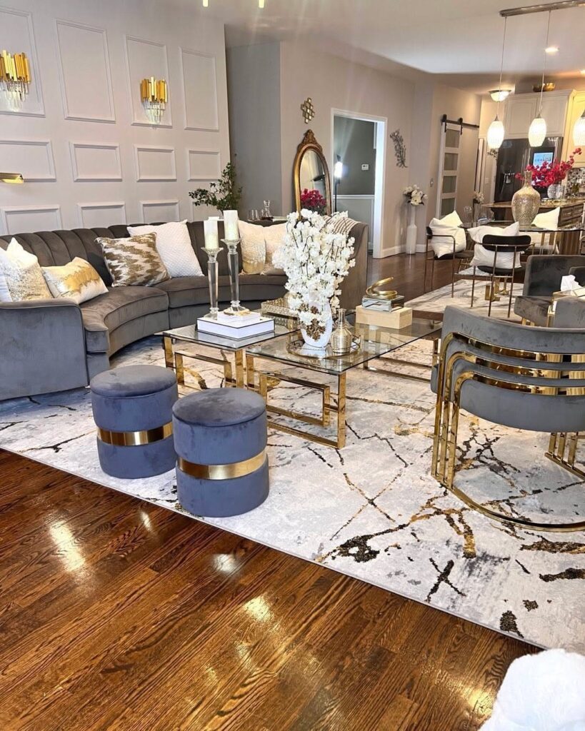 Glamorous living room with grey velvet furniture, gold accents, and a marble-patterned rug.