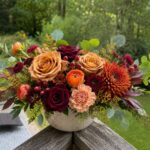 Autumn floral arrangement with orange and red roses in a white ceramic bowl.