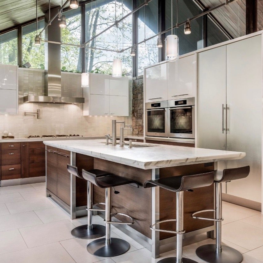 Stainless steel kitchen hood in a modern kitchen with marble island and bar stools.