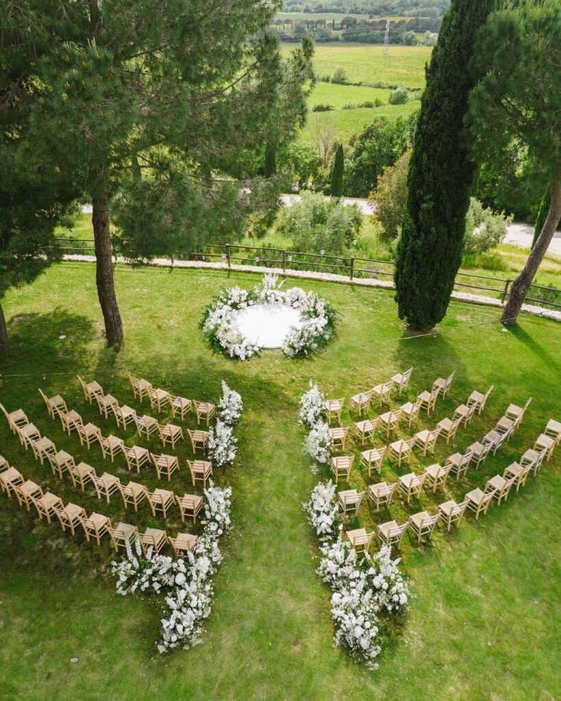 Curved wooden chairs and white floral arrangements for an outdoor garden wedding ceremony.