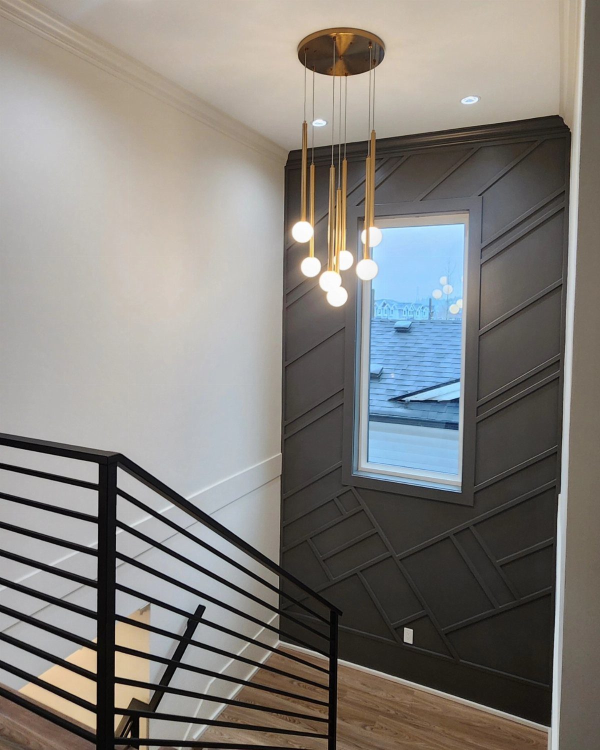 Dark grey geometric accent wall in a stairwell with a gold pendant light.